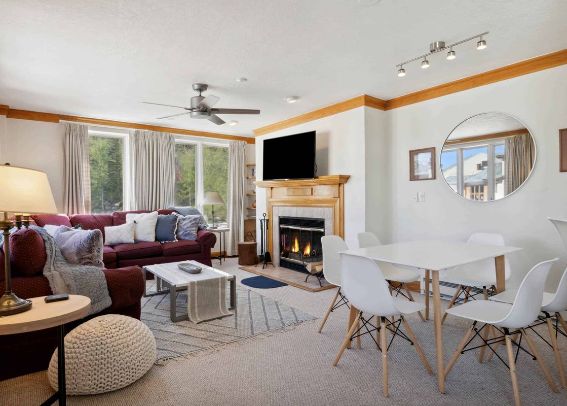 A cozy living room at The Charter L222 with a red sofa, fireplace, dining table, and large windows with an outdoor view.