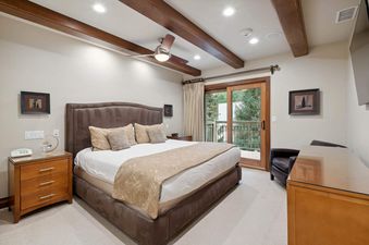 A bedroom with a king-sized bed, a wooden nightstand, and a sliding glass door that leads to a balcony overlooking a forest.