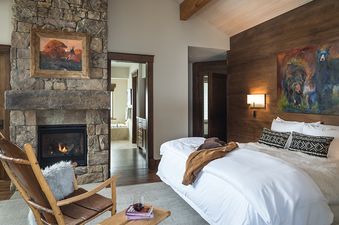 A master bedroom at Paintbrush Retreat, featuring a stone fireplace, a king-size bed, and a doorway leading to a spacious bathroom with a soaking tub.