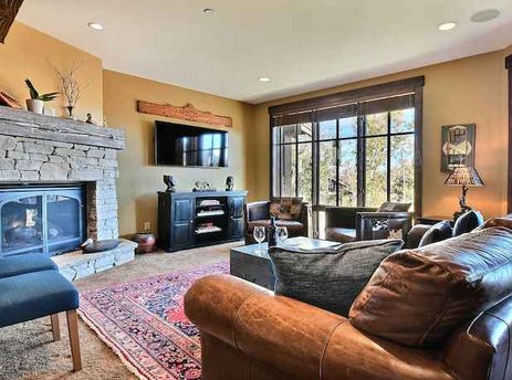 A cozy and elegantly furnished living room at Silver Star 102 features a large stone fireplace, comfortable sofas, and expansive windows showcasing an outdoor view.