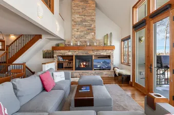 Cozy living area in Ascent at Aspen Ridge featuring a large stone fireplace and comfortable grey seating.