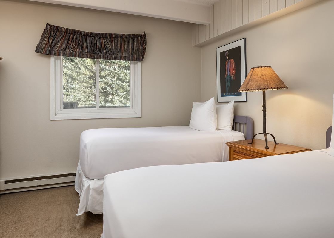 A secondary bedroom at Vantage Point 313 features two twin beds, a wooden nightstand with a lamp, and an armoire, all within a cozy, carpeted space with a window offering a view of greenery.