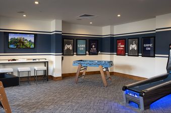 A game room at Buck Mountain 3 Bedroom One Steamboat Place 307 with a TV displaying a video game, a foosball table, and a skeeball machine, along with gaming-themed artwork on the walls.