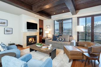 The living room in the Lumiere One Bedroom Deluxe Residence features a cozy fireplace and a view of the mountains from the windows.