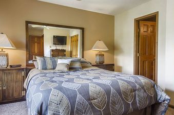 The king bedroom features a blue and white leaf-patterned duvet on the king-sized bed, flanked by wooden nightstands with rustic lamps.