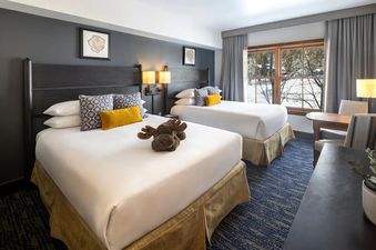 Cozy hotel room at Teton Mountain Lodge and Spa featuring two queen beds, alpine-inspired decor, and a window viewing snowy trees.