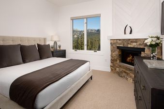 The master bedroom at Moonlight Basin 12 Wildwood features a king-size bed with a brown throw blanket, a fireplace, and a view of the mountains.