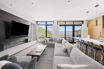 Modern open-concept living room and kitchen in One Snowmass East 603 featuring a large grey sectional, flat-screen TV, fireplace, and scenic mountain views.