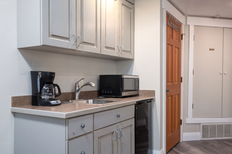 The mini kitchen area features gray cabinets, a coffee maker, a microwave, a small sink, and a mini-fridge, with a brown countertop.
