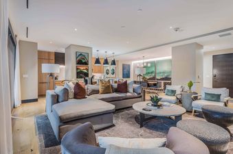 A spacious and modern living room with an L-shaped sofa, armchairs, and a coffee table, with an open-concept kitchen and dining area in the background.