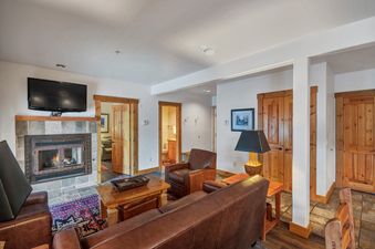 A cozy living room in the Mountain Lodge One Bedroom Deluxe Condo with a fireplace, leather furniture, and wooden accents.