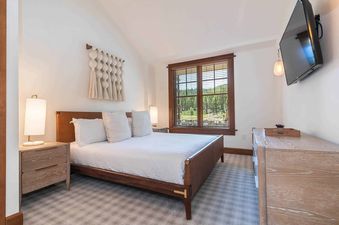 A bedroom with a king size bed, a window with a view of trees, and a TV on the wall.