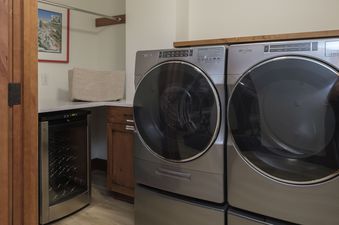 A laundry room with a washer and dryer, a wine cooler, and a shelf above the washer and dryer.