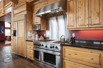 A rustic yet modern kitchen at Solamere Home featuring custom wooden cabinetry, a professional stainless steel range, dark granite countertops, and flagstone flooring.