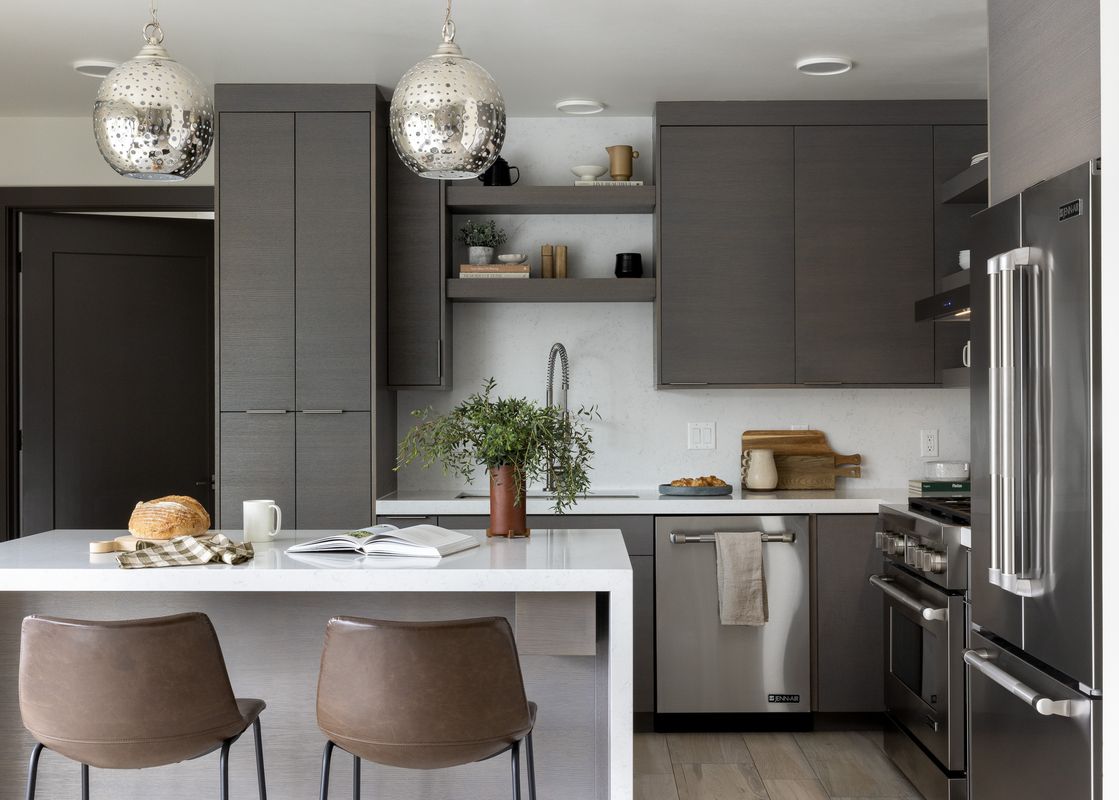 A modern kitchen in Penthouse on Glenwood 401 with dark wood cabinets, white quartz countertops, stainless steel appliances, and a kitchen island with two leather bar stools.