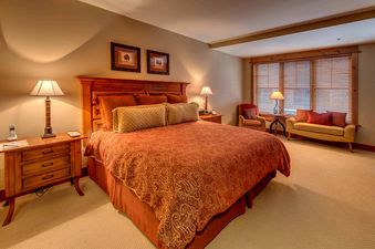 A bedroom with a king-sized bed, a wooden nightstand with a lamp, and two framed pictures on the wall.