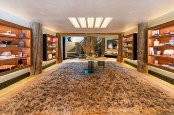 The grand living space in Northstar Chalet features a large brown shag rug, natural wood pillars, built-in bookshelves, a central glass table, and a cozy seating area under a bear artwork.