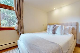 The bedroom at Villa Valhalla 9 with a comfortable bed, large window overlooking trees, and soft lighting.