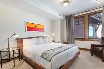 The king-sized bed in Grand Lodge Three Bedroom 301 is dressed in crisp white linens and a cozy blanket, inviting guests to relax in this spacious and well-lit room.