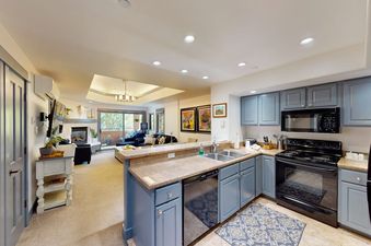 A modern kitchen with blue cabinetry and granite countertops overlooking a cozy living room in Canyon Creek B304.