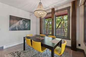 A modern dining area in Lupfer Unit D with a dark wooden table, six yellow chairs, a large beaded chandelier, and a black and white bear artwork on the wall.