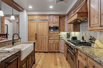 A spacious kitchen with light wood cabinetry, granite countertops, and stainless steel appliances, featuring a large gas range and a white farmhouse sink.
