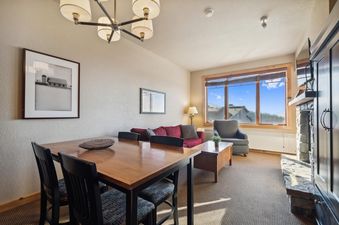 A welcoming living and dining area in Morning Eagle 209 with a wooden dining table and chairs, a red sofa, an armchair, and a large window overlooking the outdoors.