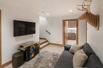 A cozy game room featuring a Pac-Man arcade machine, a comfortable sofa, and a staircase leading to another level.