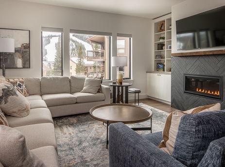 A cozy and inviting living room in Beaverhead Condo 301 features a sectional sofa, coffee table, and fireplace, with large windows overlooking a snow-covered mountain.