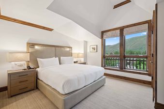 The Aspen 30B bedroom features a king bed, a plush headboard, two nightstands with lamps, and a large window overlooking the mountains.