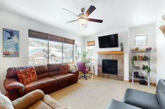 The living area features a comfortable brown leather sofa, a fireplace, and a flat-screen TV, with large windows offering a snowy outdoor view.