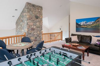 A spacious games room with a foosball table, a board game table, and a comfortable leather sofa next to a large stone pillar.