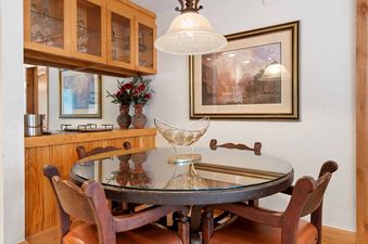A close-up view of the dining area inside The Charter D2705, featuring a round glass-top table with wooden chairs, an elegant overhead light fixture, and a framed landscape painting on the wall.