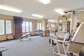 A well-equipped fitness center with various exercise machines, dumbbells, and large windows offering an exterior view.