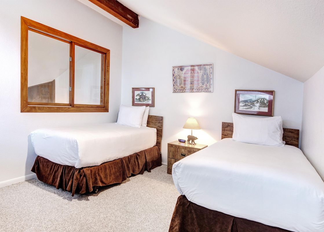 A cozy guest bedroom with two twin beds, white linens, and rustic wooden furniture.