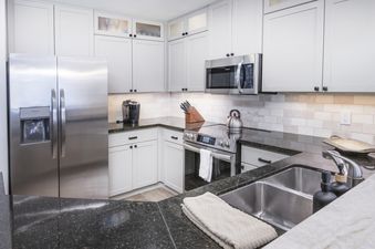 A modern kitchen at Highlands Slopeside in Beaver Creek features light gray cabinetry, dark granite countertops, and stainless steel appliances, including a refrigerator, microwave, and electric range.