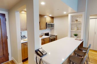 A modern kitchen with white countertops and a breakfast bar with three stools.