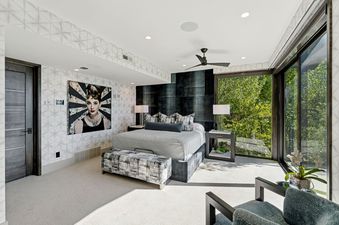 A primary bedroom at Star Gazer at Deer Valley features a king-sized bed, stylish nightstands, a pop art portrait of Audrey Hepburn, and floor-to-ceiling windows with green tree views.