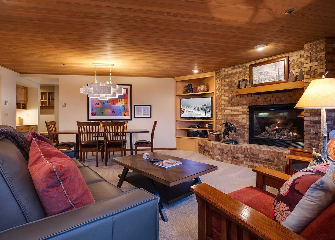 A cozy living room in Chateau Chamonix CX123 with a large leather sofa, a brick fireplace, a television, and a dining area under a modern chandelier.