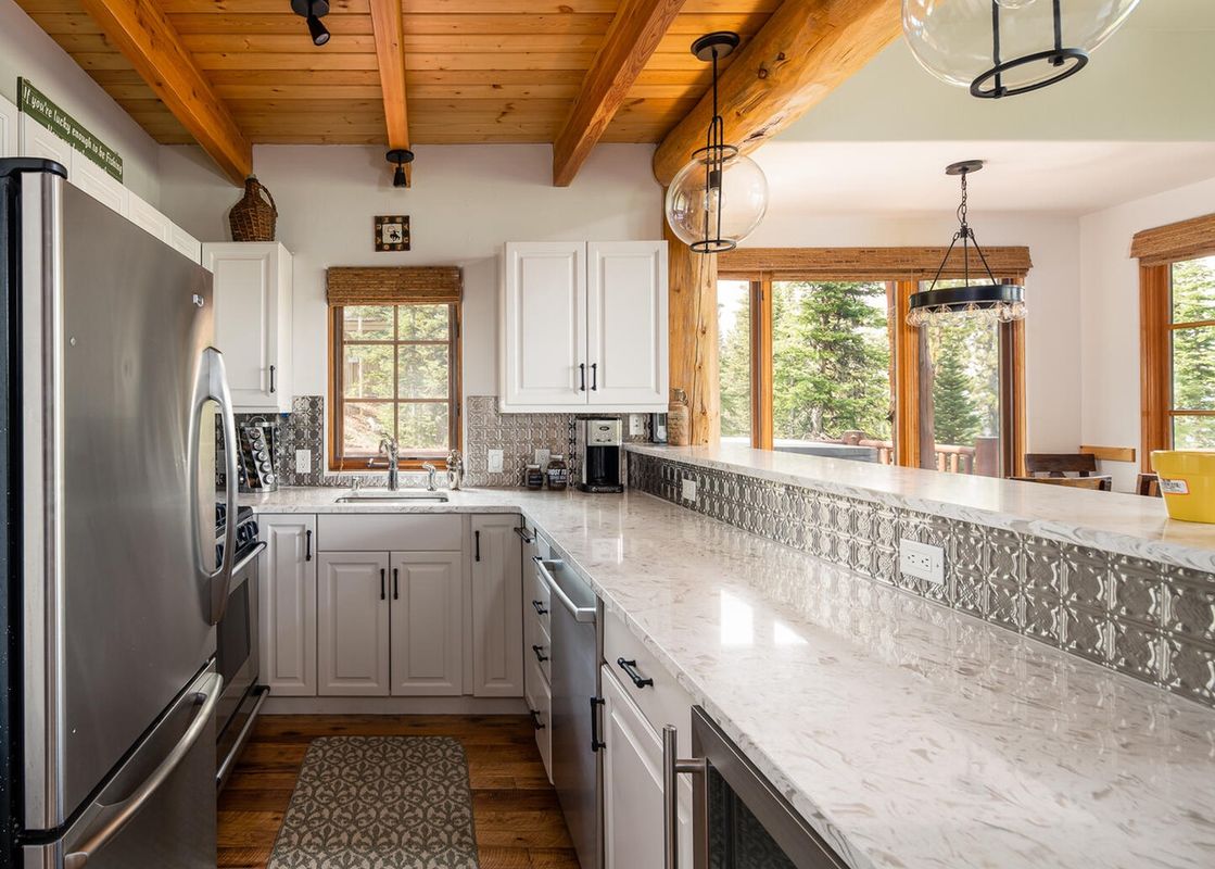 Moonlight Basin 7 Gambler kitchen features white cabinetry, stainless steel appliances, a farmhouse sink, and granite countertops.
