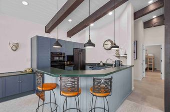A modern kitchen at Enclave 313 with blue and gray cabinetry, dark green countertops, and exposed wooden beams on the vaulted ceiling.