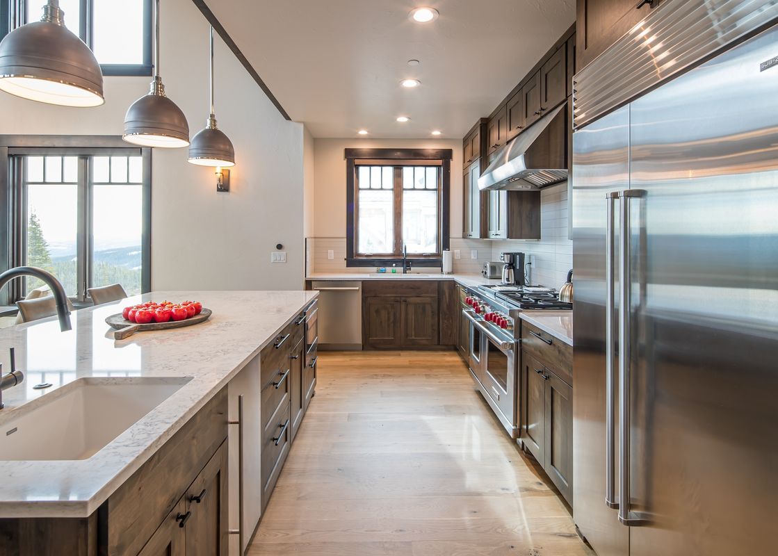 A modern kitchen at 7 Lower Cascade Ridge with dark wood cabinetry, stainless steel appliances, and a large island with a sink, all brightly lit by pendant and recessed lighting.