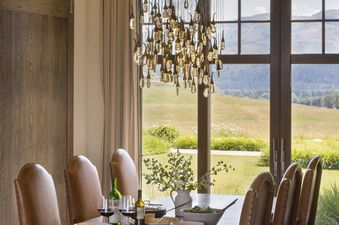 Elegant dining area at Le Refuge with leather chairs and a unique chandelier overlooking scenic hills.