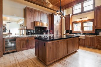 A luxurious kitchen with rich wood cabinetry, a dark granite island, stainless steel appliances, and large windows, exuding warmth and modern elegance.