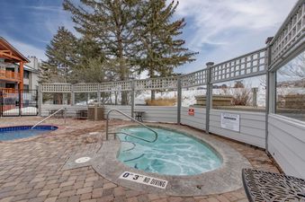 An inviting outdoor hot tub with clear water and bubbling jets, surrounded by brick paving and a wooden fence, awaits guests at Snow Flower 129 Park City.