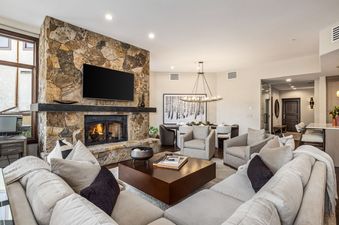 A cozy and elegant living room with a large stone fireplace, a sectional sofa, a coffee table, and an adjacent dining area.