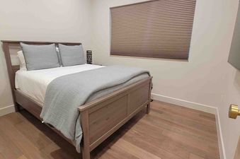 A serene bedroom at 1175 B Casolar Del Norte with a light wood bed, white and gray bedding, a window with blinds, and a wall-mounted TV.