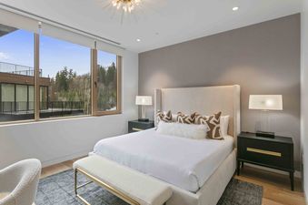 The bedroom features a large window offering expansive views of the wooded landscape and a modern building exterior.