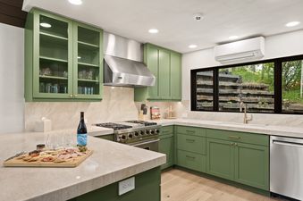 A modern kitchen in Onyx Lodge with sage green cabinetry, marble countertops, stainless steel appliances, and a window overlooking a lush outdoor landscape.