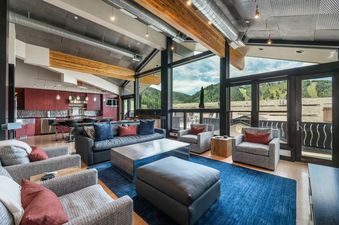 A spacious living room with large windows overlooking a mountain view, featuring a comfortable sectional sofa, armchairs, a coffee table, and a rug.